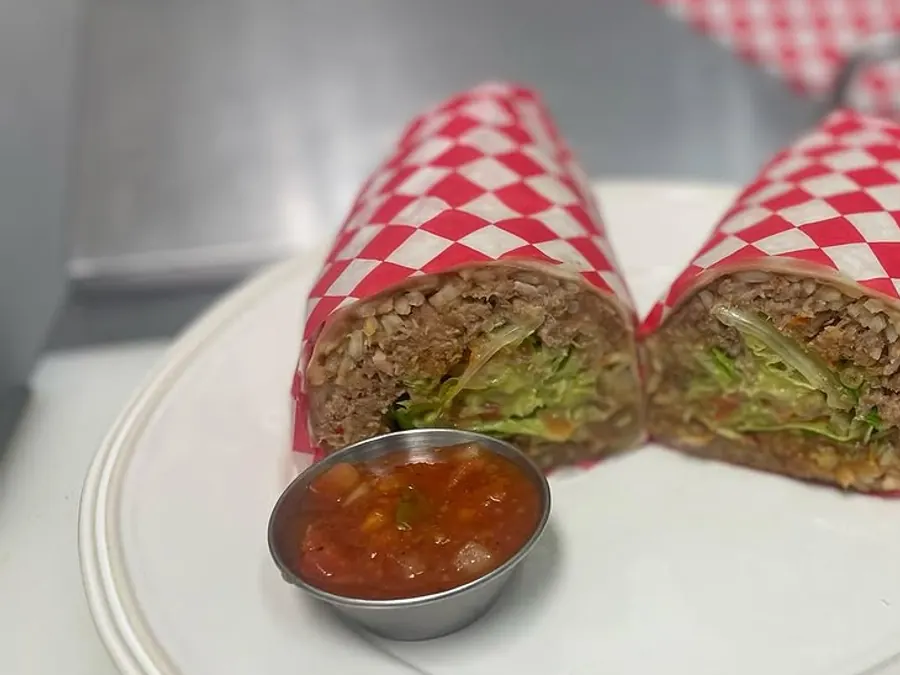 A stuffed burrito cut in two, served with a cup of roasted tomato salsa