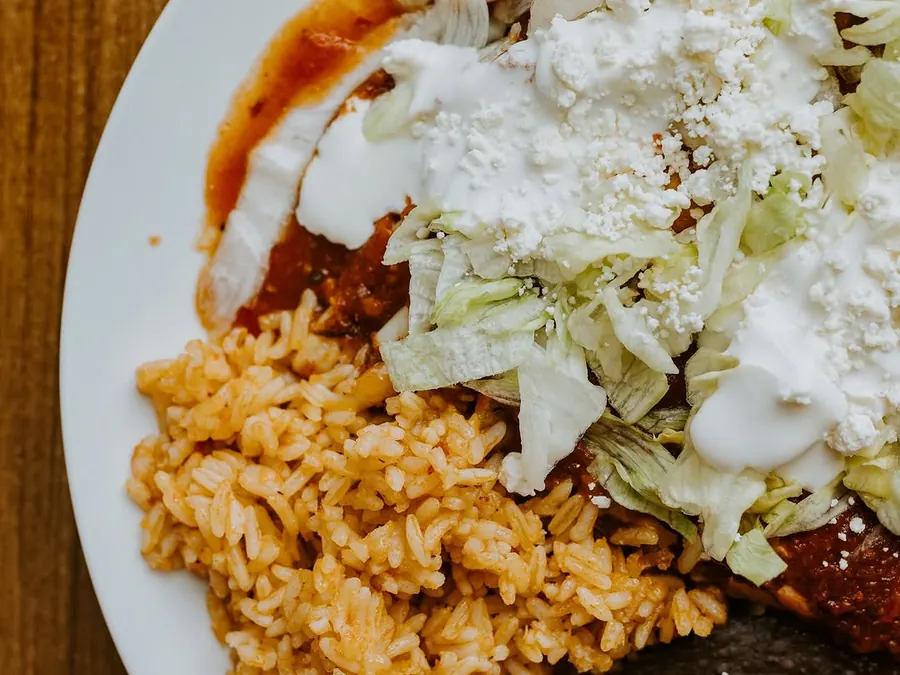Enchiladas under crema and queso fresco, plated with Mexican rice and refried beans