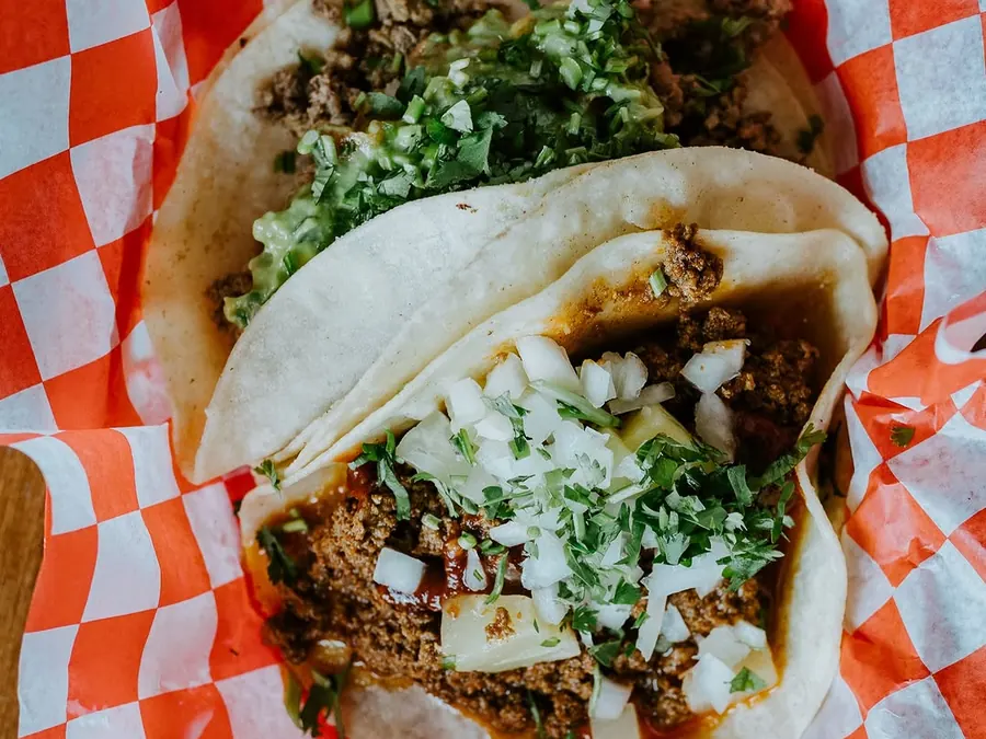 Two street tacos with cilantro and onion in a red-checkered basket
